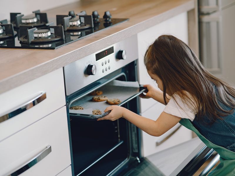 Copil punând tava cu biscuiți la cuptor